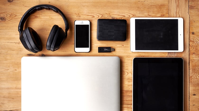 Notebook, tablets, celular e fone de ouvido em cima de uma mesa de madeira