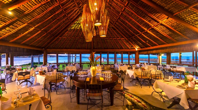 Imagem de um restaurante com diversas mesas e cadeiras de frente para o mar.
