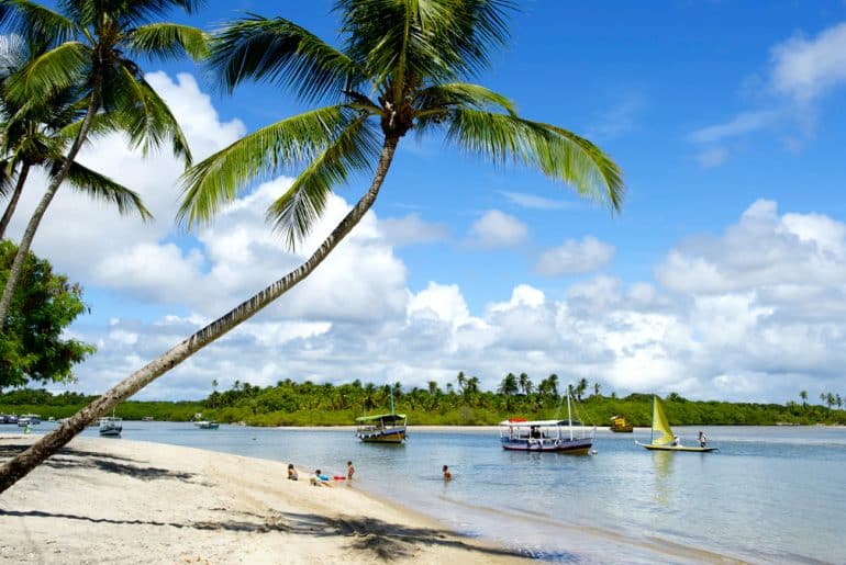 5 roteiros de viagem incríveis no Nordeste brasileiro Foto de uma praia no nordeste com embarcações e natureza ao fundo