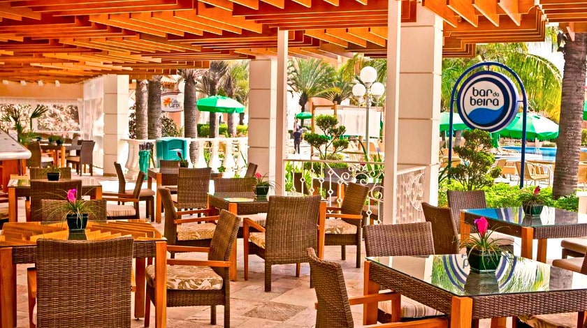 Imagem de um restaurante/bar com diversas mesas e cadeiras ao ar livre.