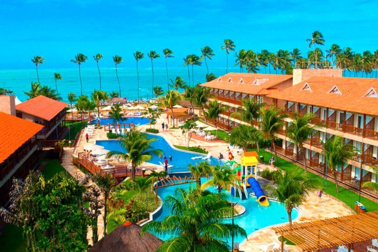 Foto do resort com acomodações, piscina ao centro e praia ao fundo